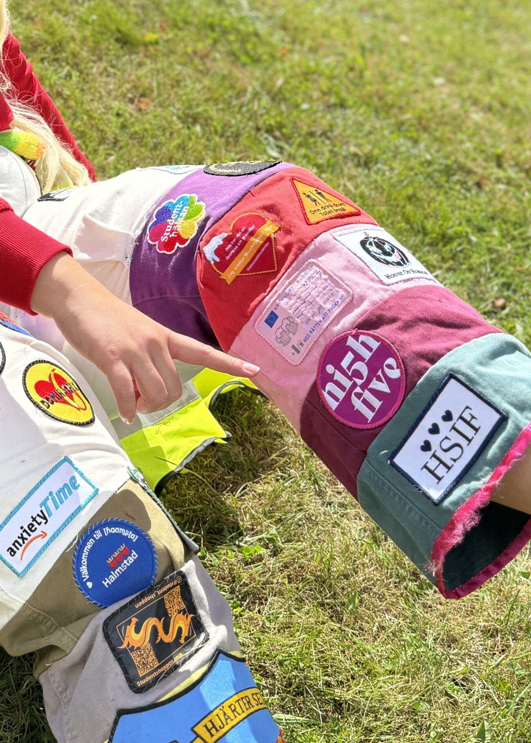 Färgglada studentoveraller med tygmärken, där ett rosa HighFive märke syns tydligt.