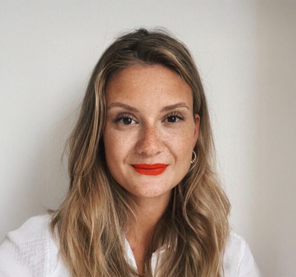 Blond kvinna i vit skjorta med ljus bakgrund, hennes läppar är målade i rött läppstift.